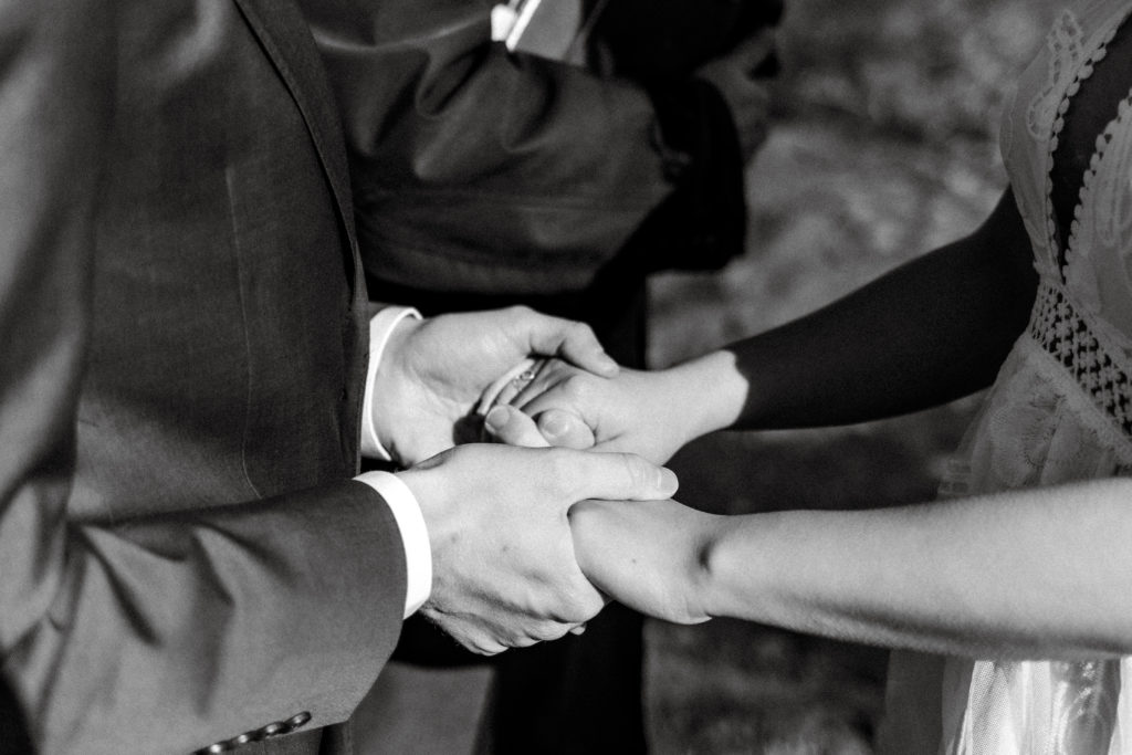 An up-close shot of the couple's hands during the ceremony, featuring the bride's new ring on her ring finger.