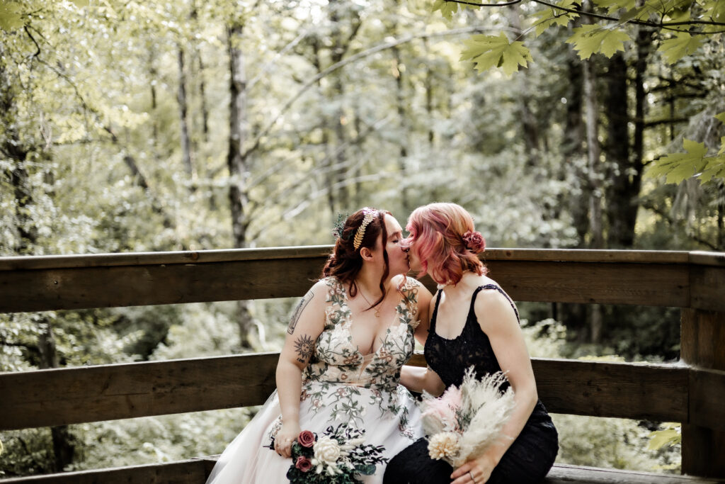 Brides share a kiss on the bench at their forest elopement in Langley