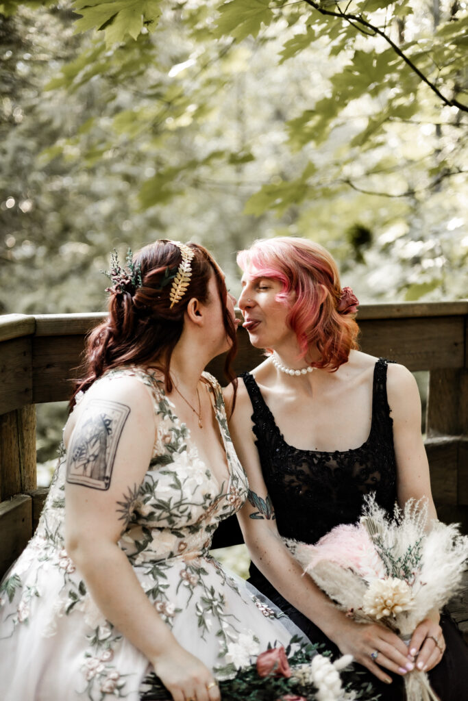 Brides touch their tongues together at their forest elopement in Langley