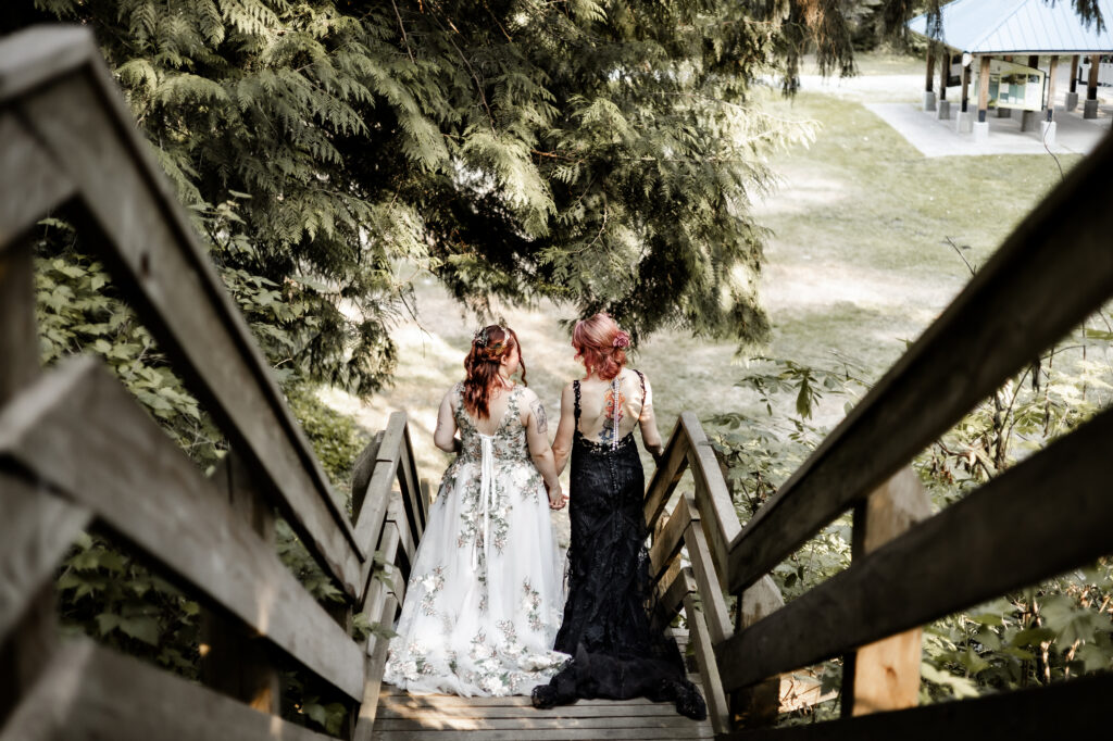 Brides hold hands and walk down the stairs together at their forest elopement in Langley