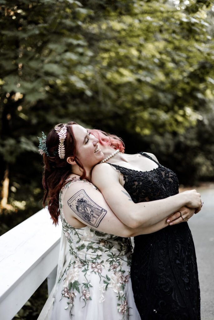 One bride hugs the other from behind at their forest elopement in Langley