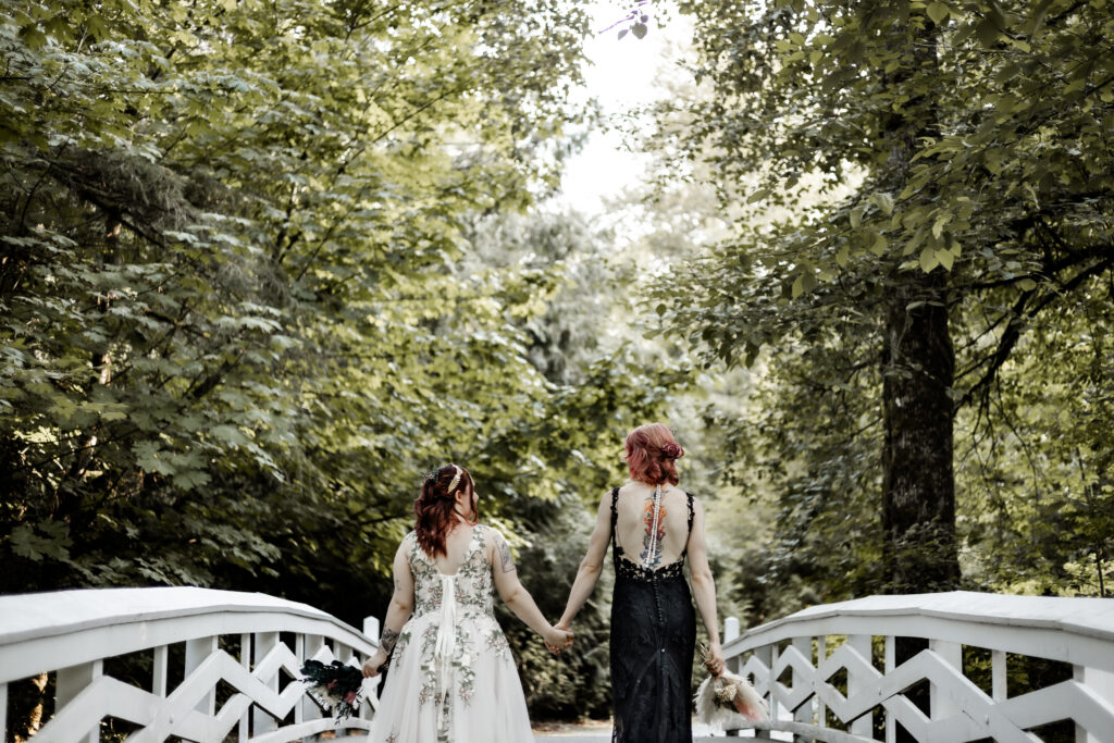 Brides hold hands and walk down a white bridge forest elopement in Langley