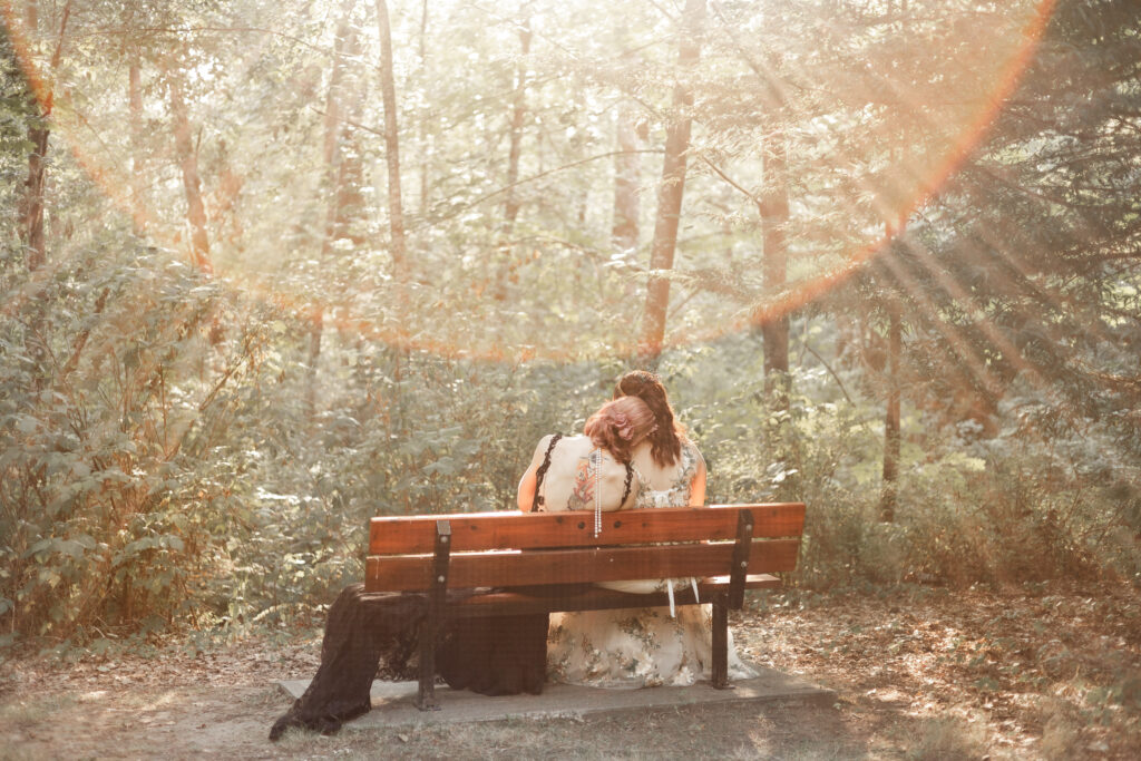 Brides sit on a bench as the sun flares at this forest elopement in Langley