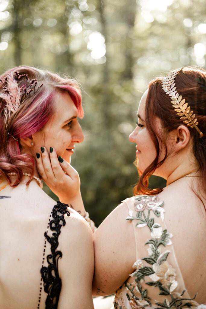 Brides look longingly into each others eye at their forest elopement in Langley