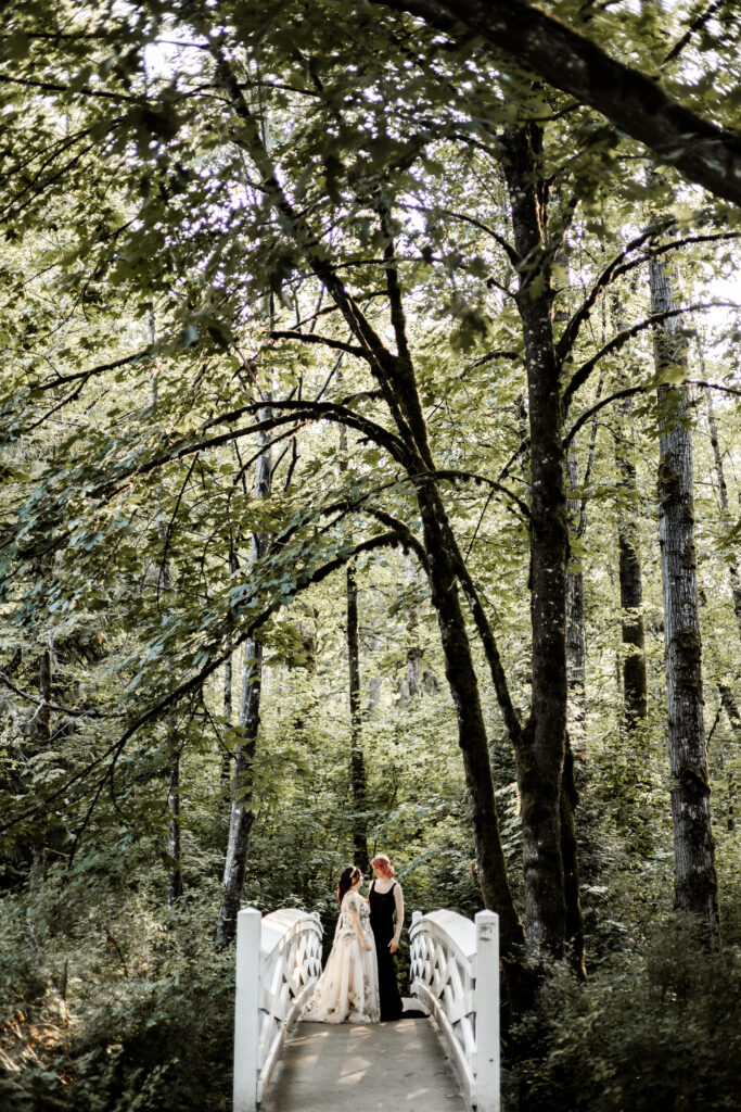 Brides stand together on a white bridge at this forest elopement in Langley