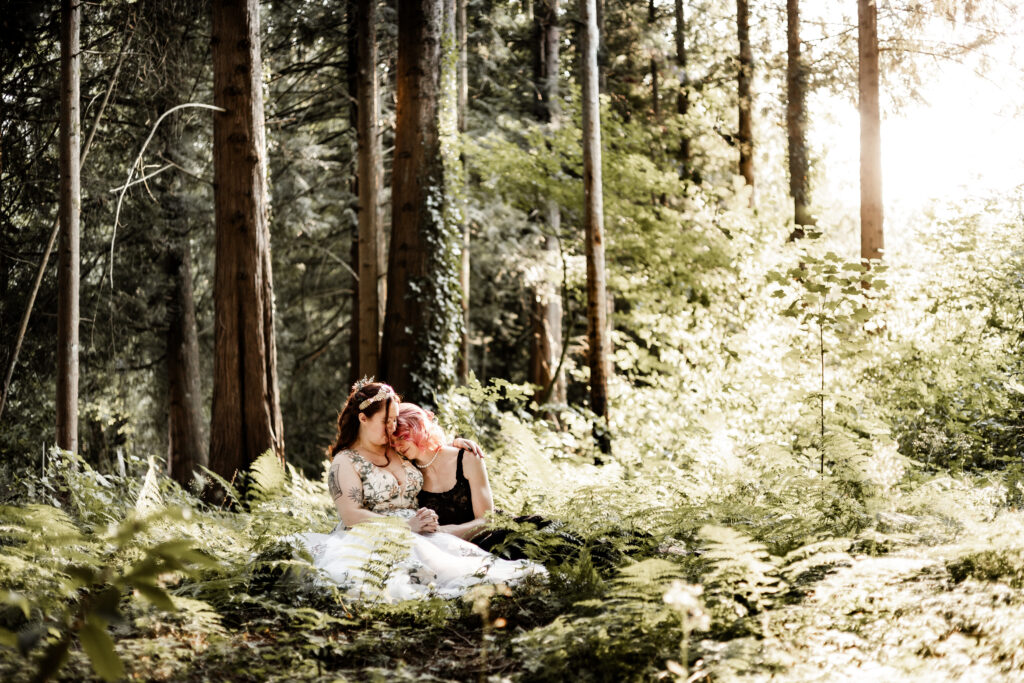 Brides cuddle together on the forest floor at their forest elopement in Langley