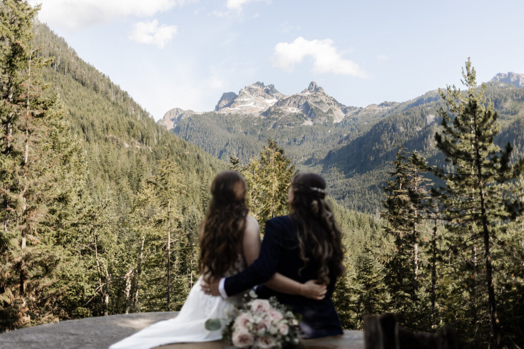 The couple have their arms around each other as they look at the Sky Pilot lookout at this Sea to Sky Gondola wedding