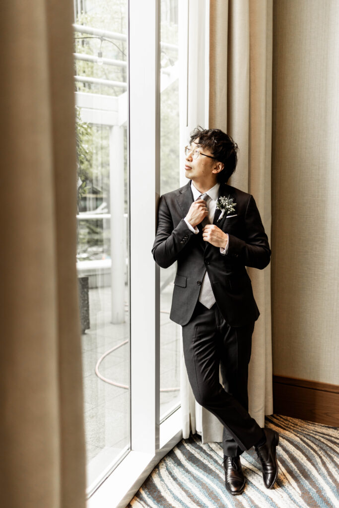 Groom adjusting his tie and looking out the window at this Marriott Pinnacle wedding