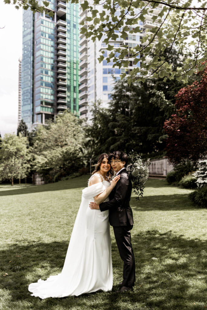 The bride and groom hold each other as they pose in front of a big building at this downtown Vancouver Marriott Pinnacle wedding