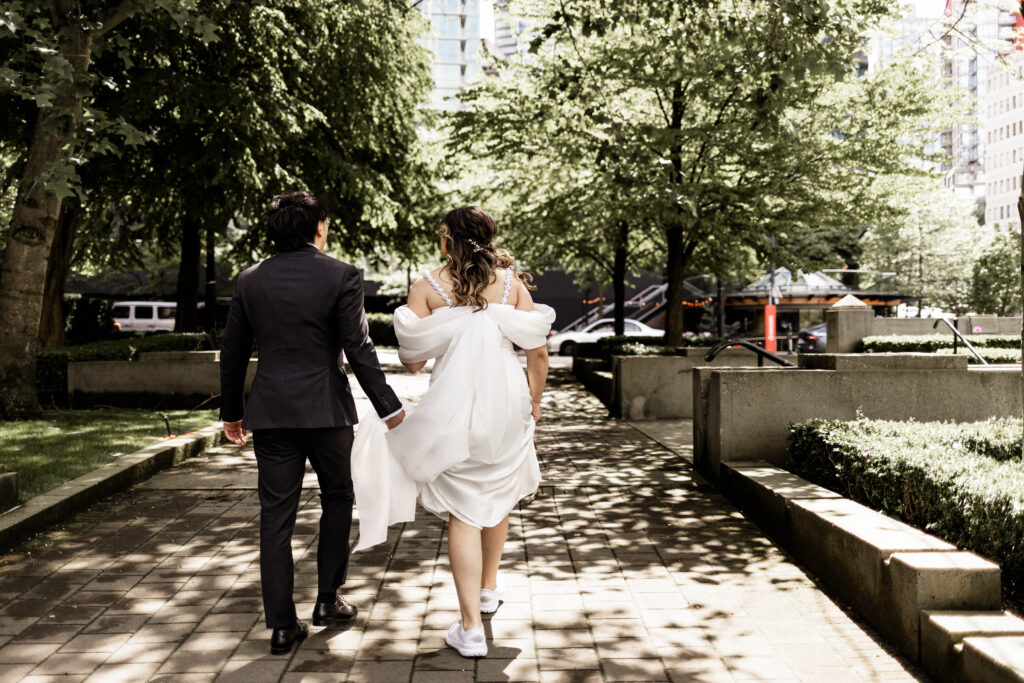 The groom holds the brides dress as they walk back to their downtown Vancouver Marriott Pinnacle wedding