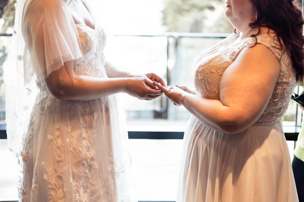 Two brides exchange rings during their ceremony, signifying the beginning of their marriage at their Black Rock Oceanfront Resort wedding.