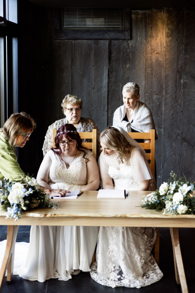 The brides and their witnesses sign the wedding papers at their Black Rock Oceanfront Resort wedding.