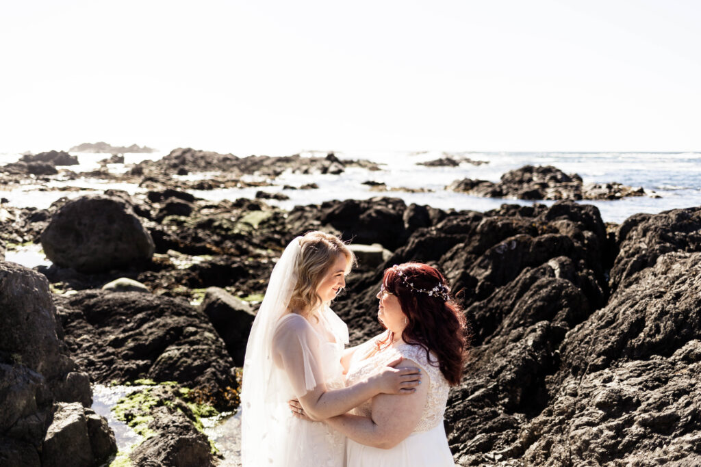 The brides pose among black rocks on the beach at their Black Rock Oceanfront Resort wedding.