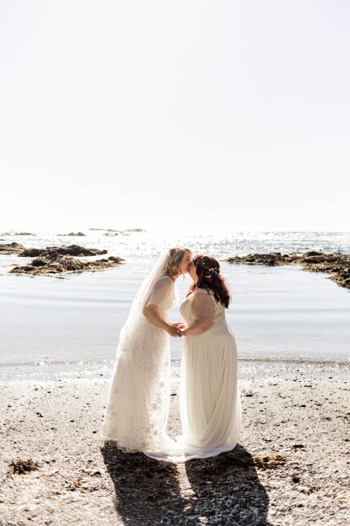 The brides lean in for a kiss at the edge of the water at Big Beach during their Black Rock Oceanfront Resort wedding.