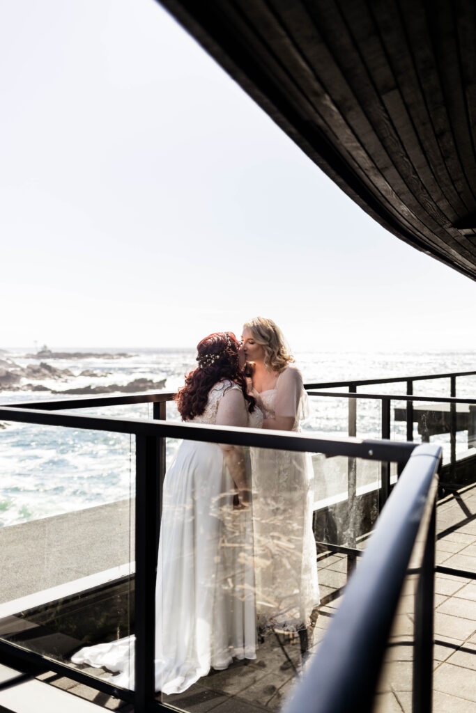 Two brides share a kiss on the patio of their hotel room at their Black Rock Oceanfront Resort wedding.