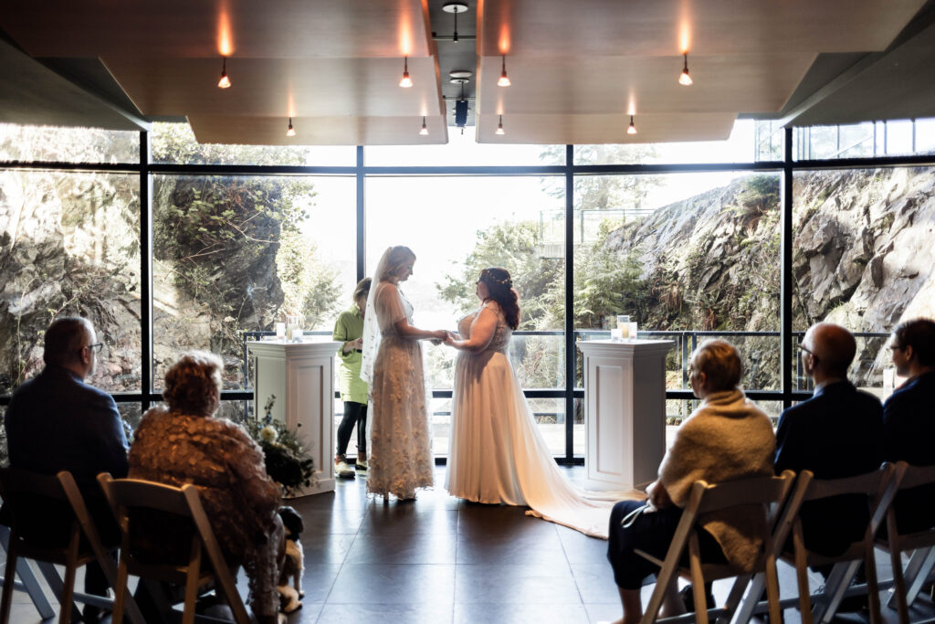 Two brides stand holding hands at the altar in the wine cellar of Black Rock Oceanfront Resort, saying their vows.