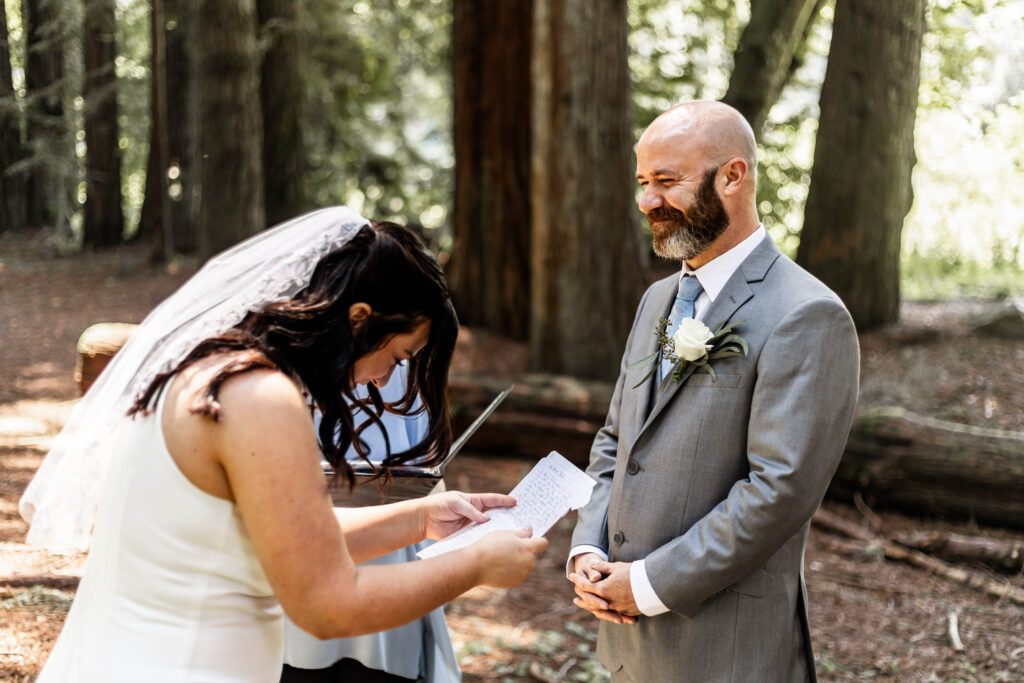 A couple shares a laugh during their vows standing amongst giant redwood trees.