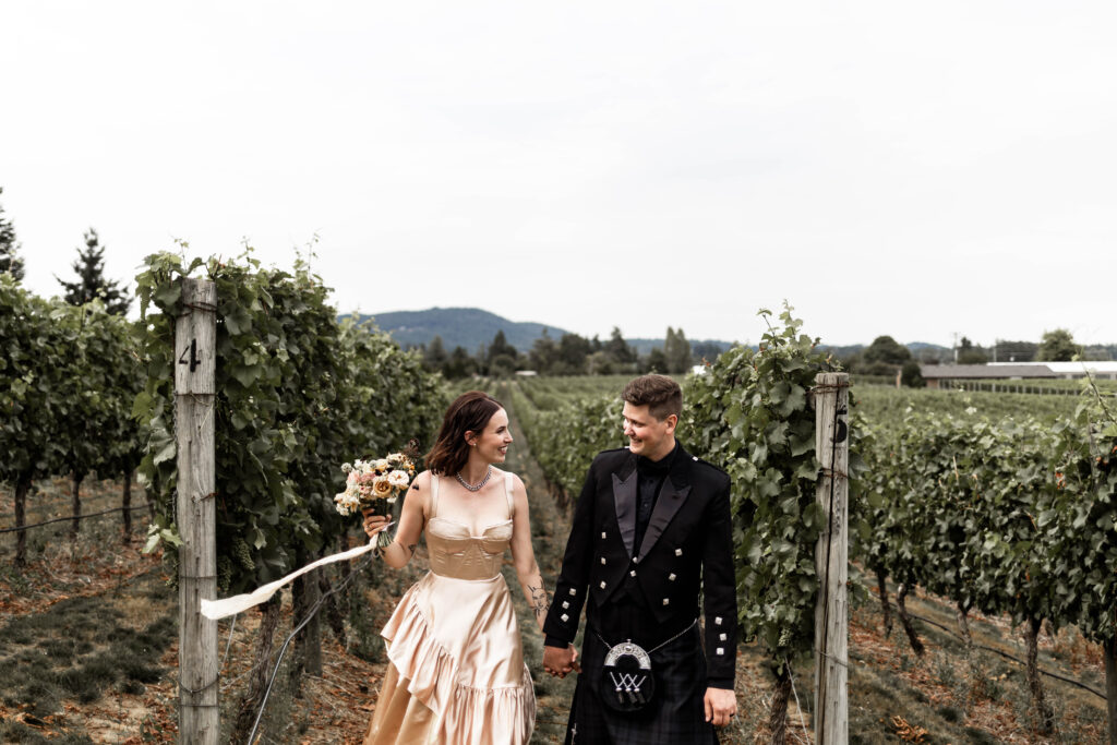 Bride and groom hold hands as they walk down the rows of the vineyard at this Church and State Winery wedding