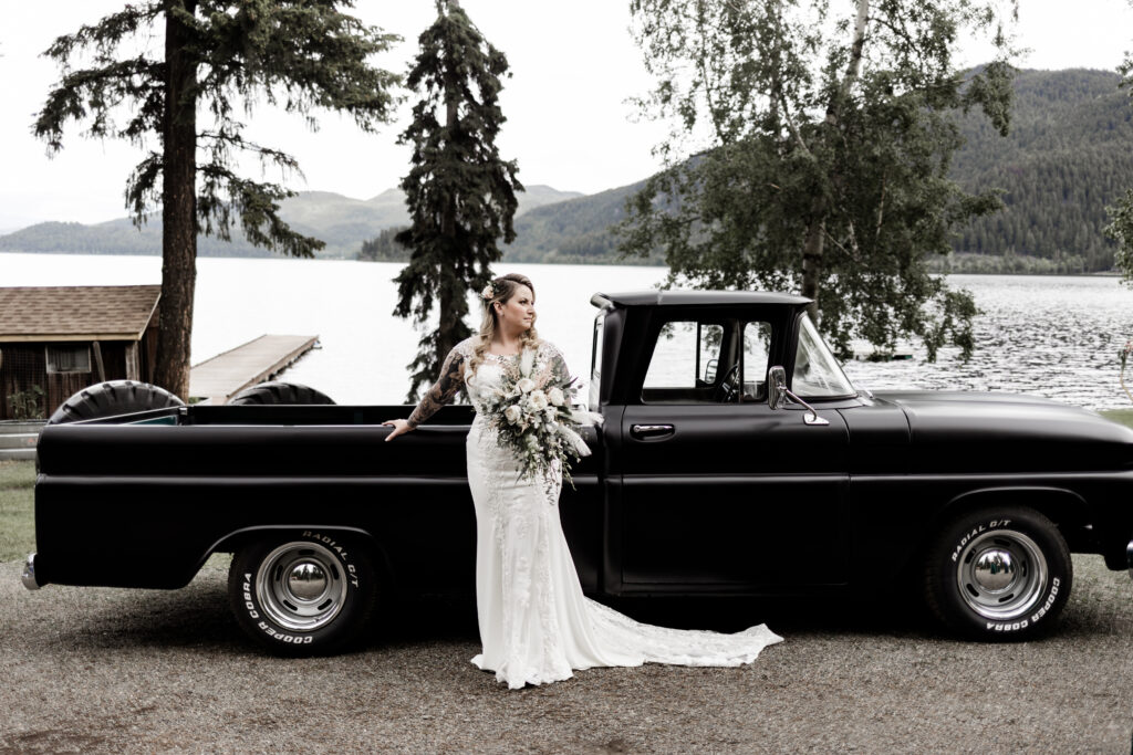 The bride poses in front of a black vintage car at this canim lake wedding