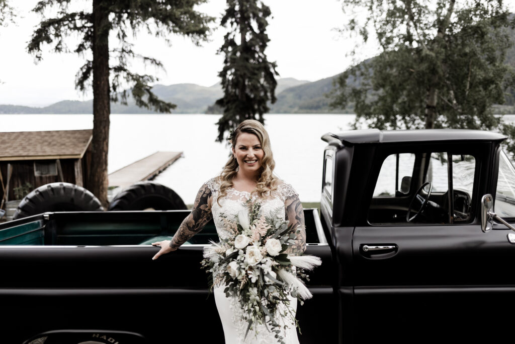 The bride poses in front of a black vintage car at this canim lake wedding