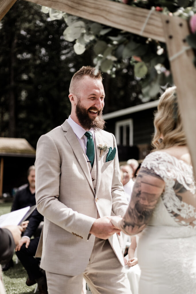 The groom smiles at his bride during the ceremony at this canim lake wedding