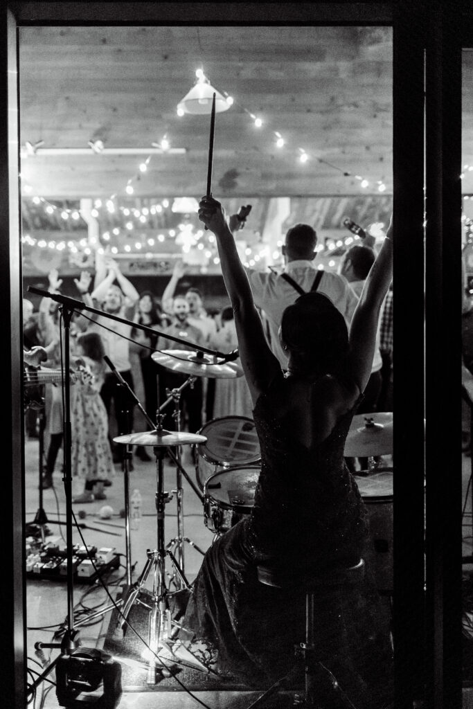 The bride raises her drumsticks in success at this A live band plays at this Gibsons Island summer camp wedding at Camp Elphinstone