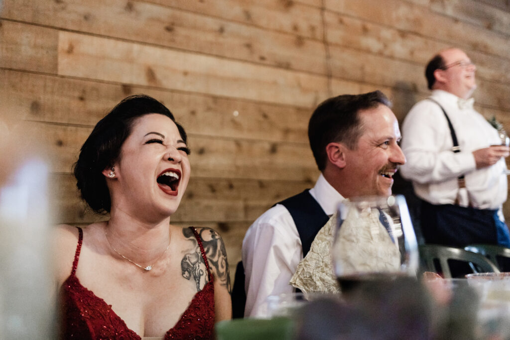 The couple laughs during speeches at their Gibsons Island summer camp wedding at Camp Elphinstone