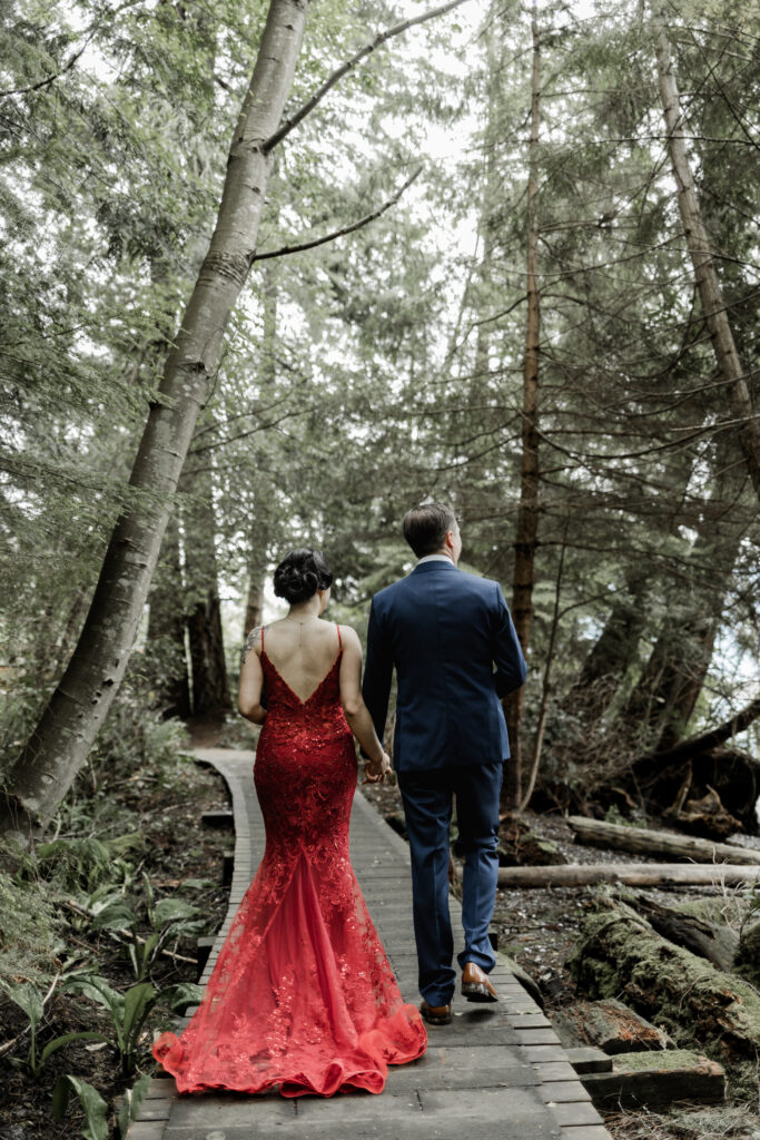 The bride and groom holds hands as they walk down a wooden boardwalk at their Gibsons Island summer camp wedding at Camp Elphinstone