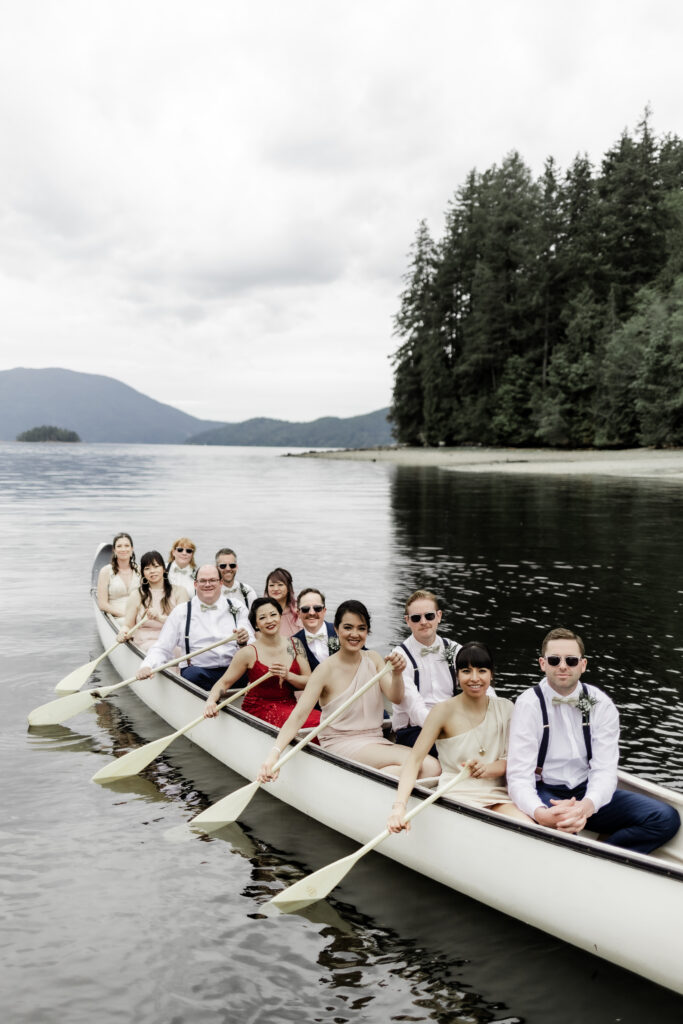 The bridal party poses in a giant canoe on the water at this Gibsons Island summer camp wedding at Camp Elphinstone