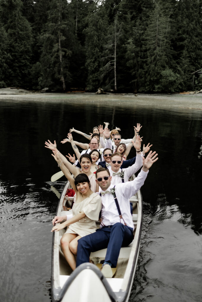 The bridal party poses in a giant canoe on the water at this Gibsons Island summer camp wedding at Camp Elphinstone