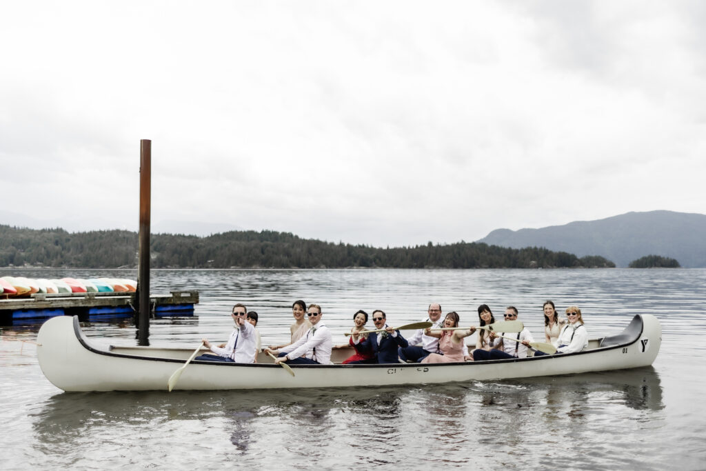 The bridal party poses in a giant canoe on the water at this Gibsons Island summer camp wedding at Camp Elphinstone