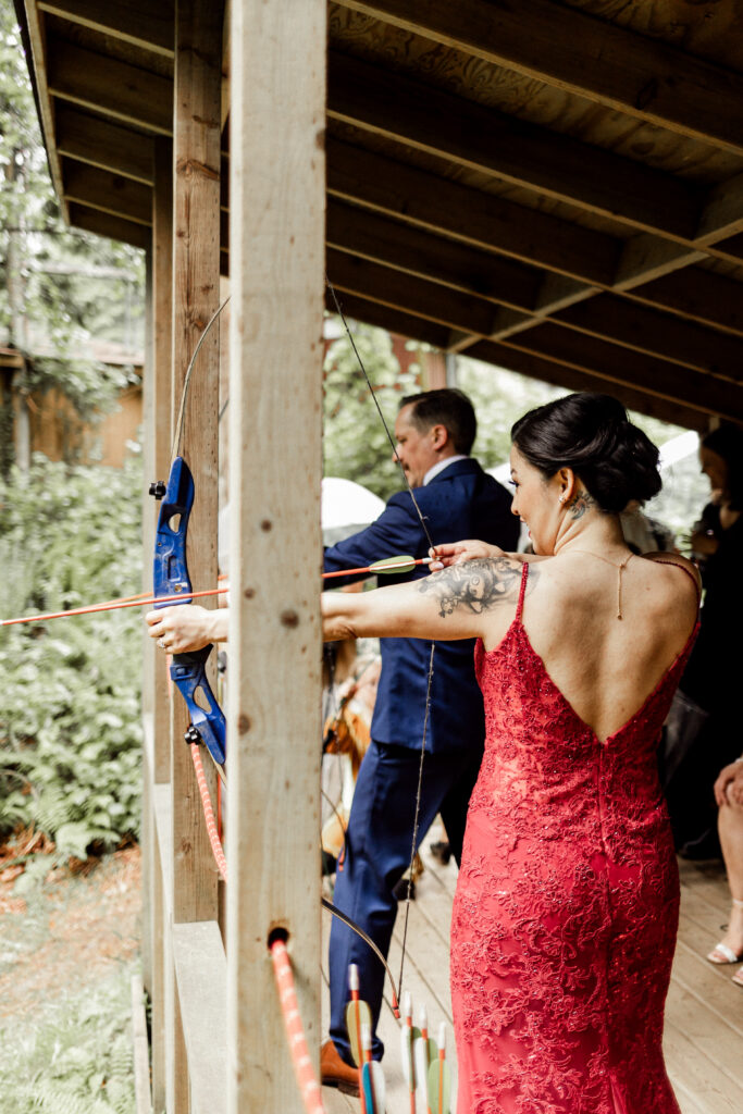 The bride and groom aim their bow and arrows the targets at this Gibsons Island summer camp wedding at Camp Elphinstone