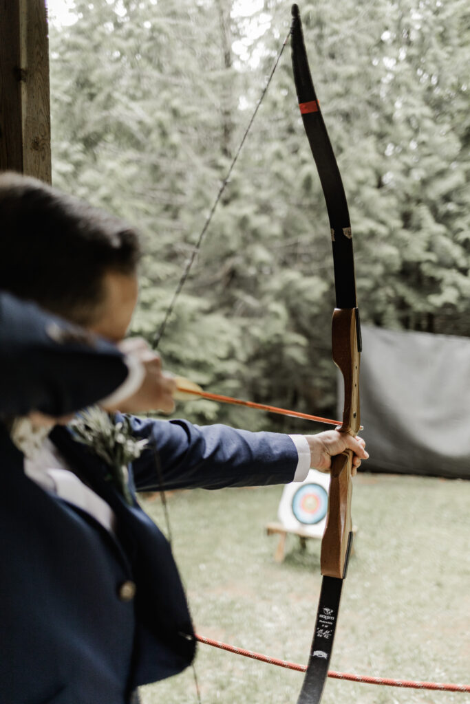 The groom aims his bow at the target at this Gibsons Island summer camp wedding at Camp Elphinstone