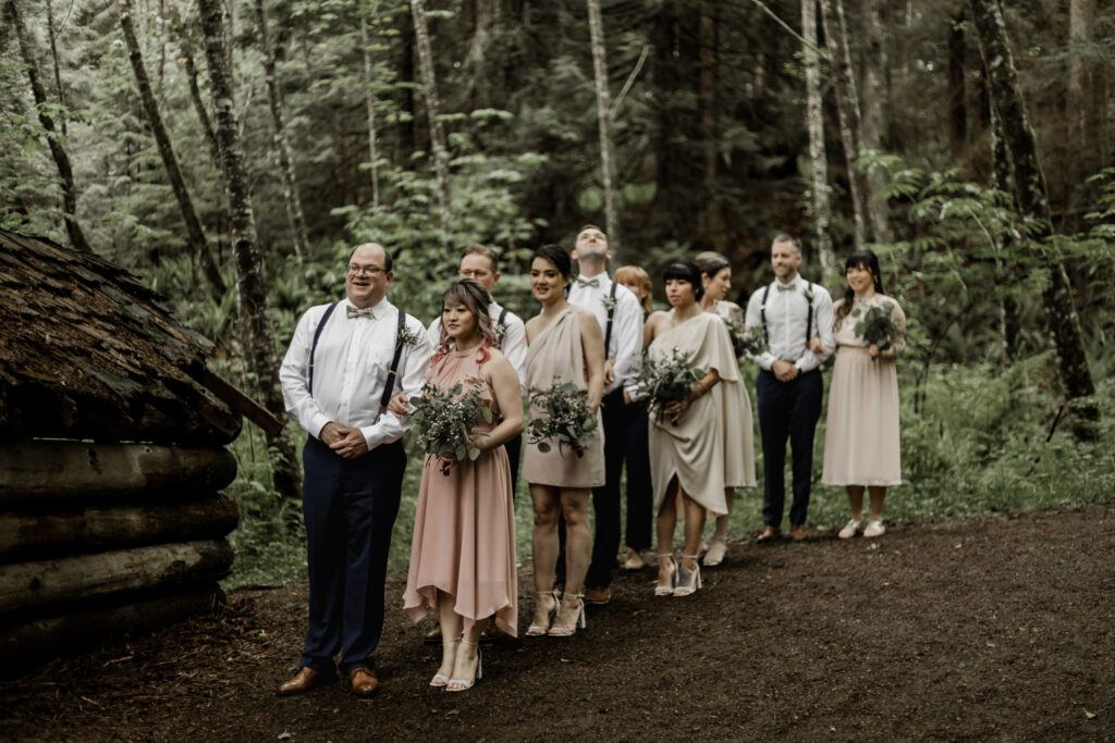 The bridal party lines up in the forest in preparation for the ceremony at this Gibsons Island summer camp wedding at Camp Elphinstone