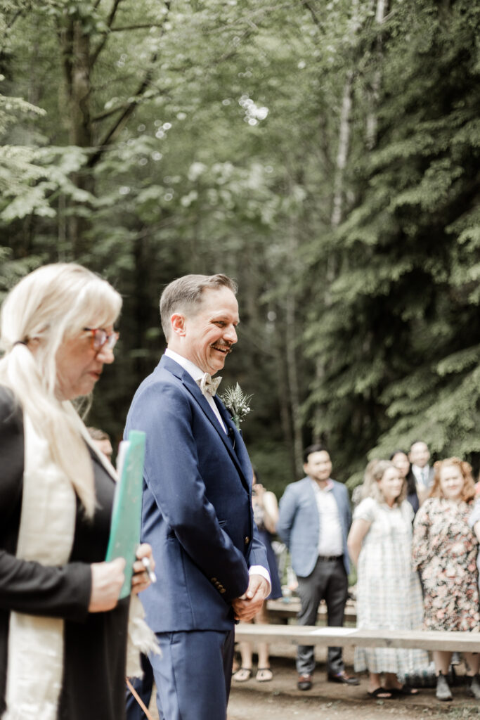 The groom smiles at his approaching bride at this Gibsons Island summer camp wedding at Camp Elphinstone