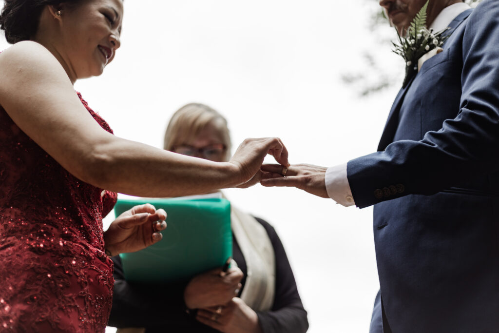 An up close of the bride and groom's hands as they exchange rings during their ceremony at their Gibsons Island summer camp wedding at Camp Elphinstone