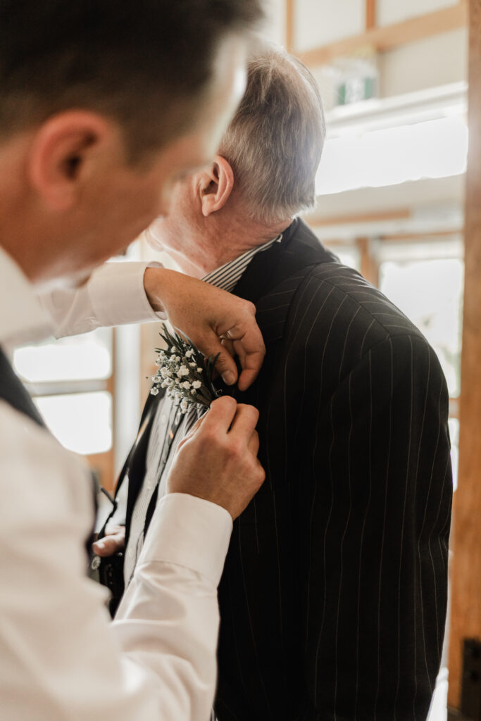 The groom pins a boutonniere on his father at this Gibsons Island summer camp wedding at Camp Elphinstone