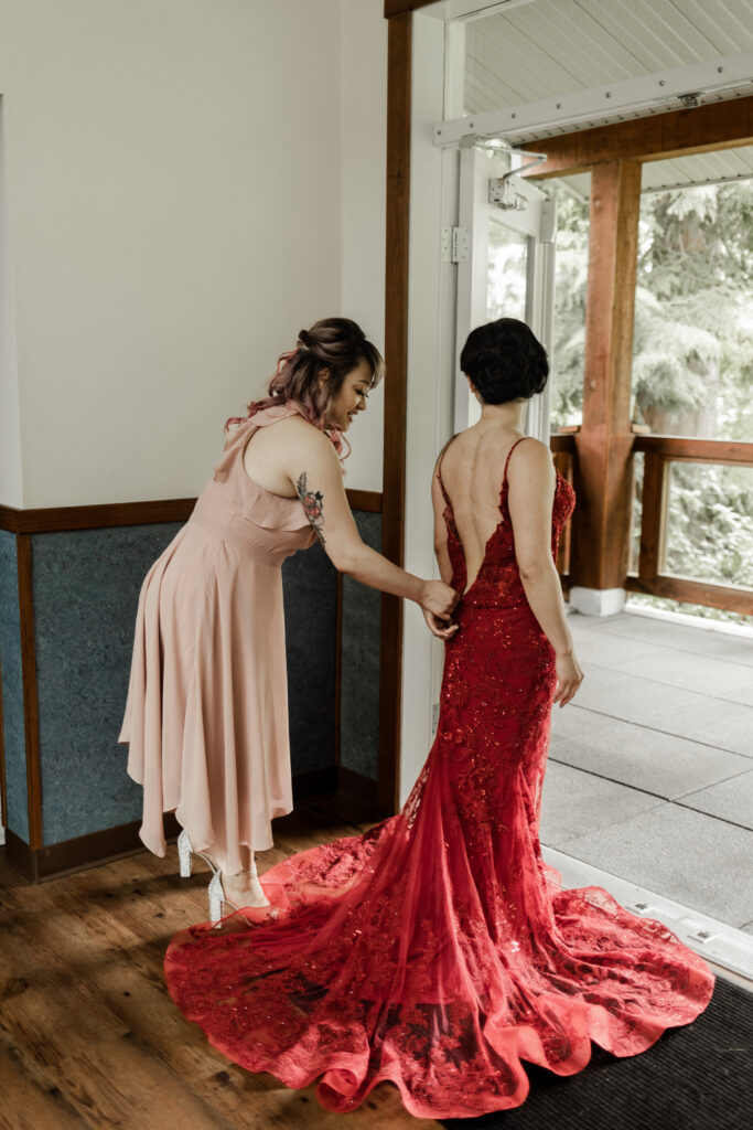 The bride gets her red dress done up by her sister at this Gibsons Island summer camp wedding at Camp Elphinstone