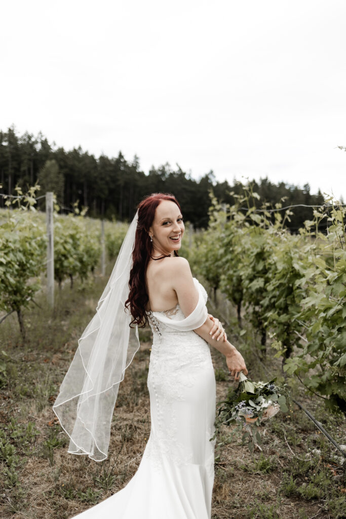 bride poses in the rows of the vineyard at this Cobble Hill Winery wedding