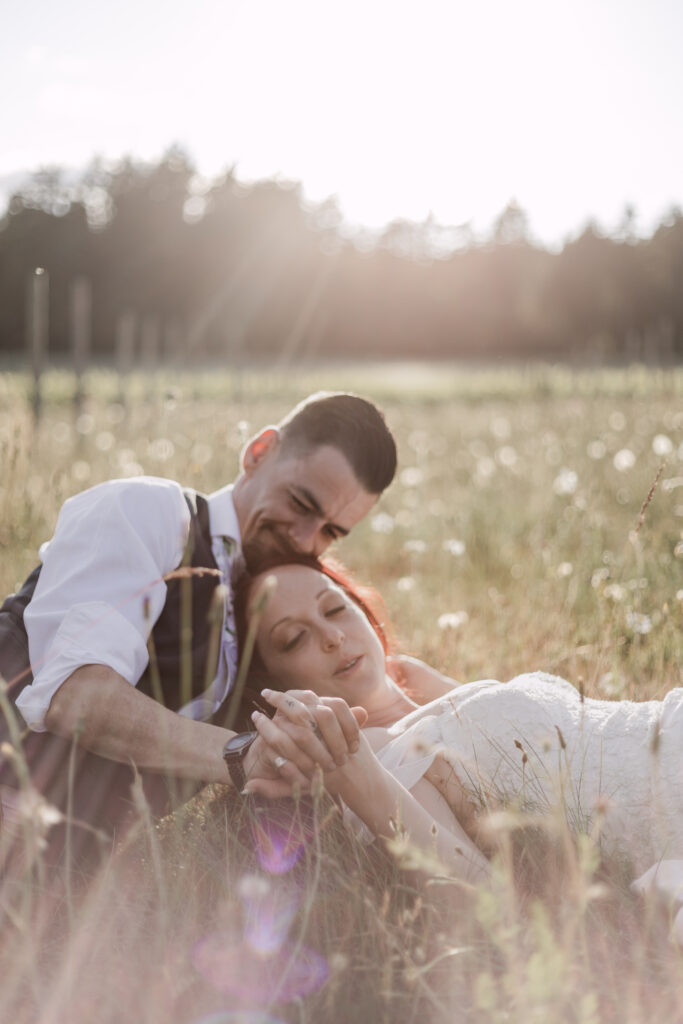 bride and groom lay down in a field during golden hour at this Cobble Hill Winery wedding