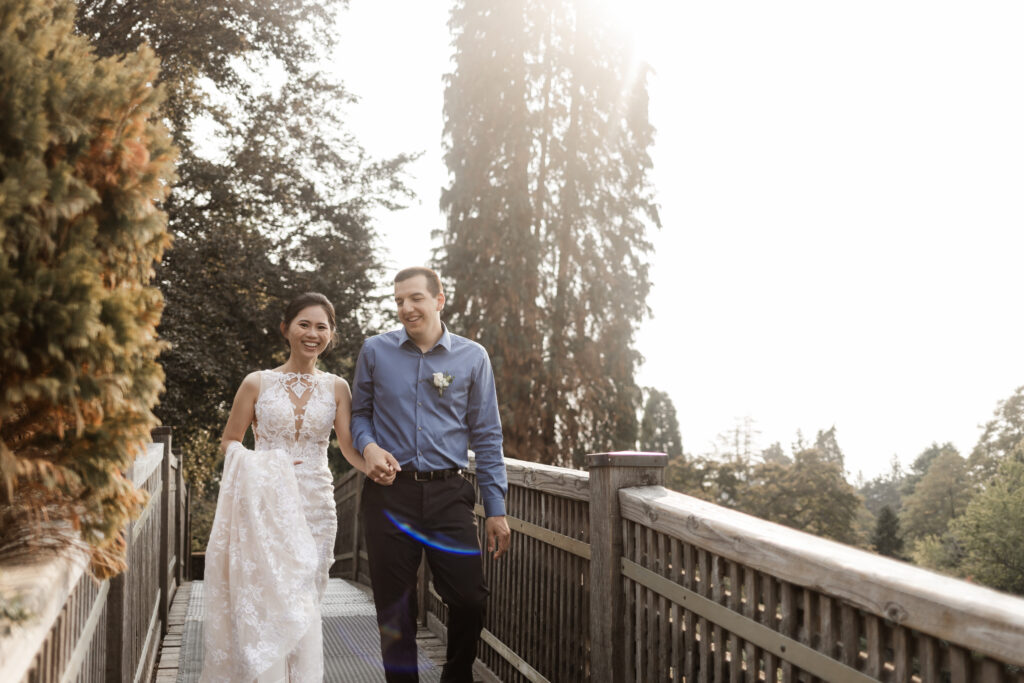 Eileen and Jeremy hold hands as they walk down a wooden bridge at this Bloedel Conservatory wedding 