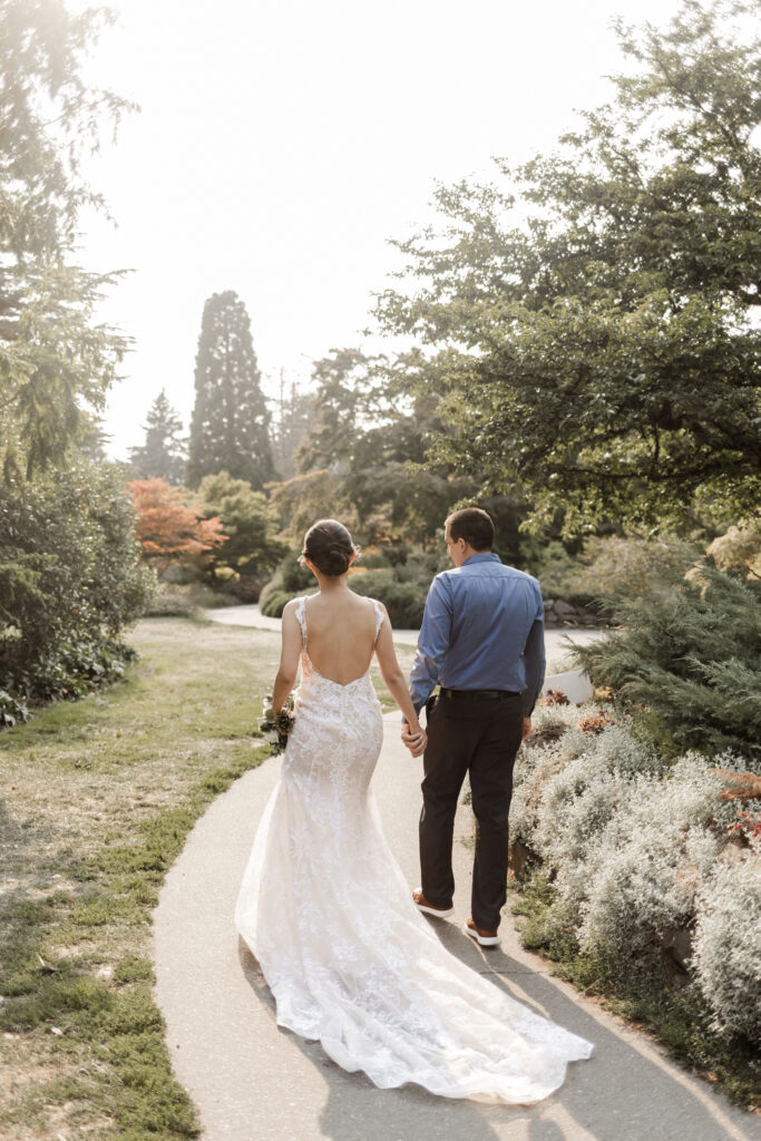 The bride and groom hold hands as they walk through the park at this Bloedel Conservatory wedding 