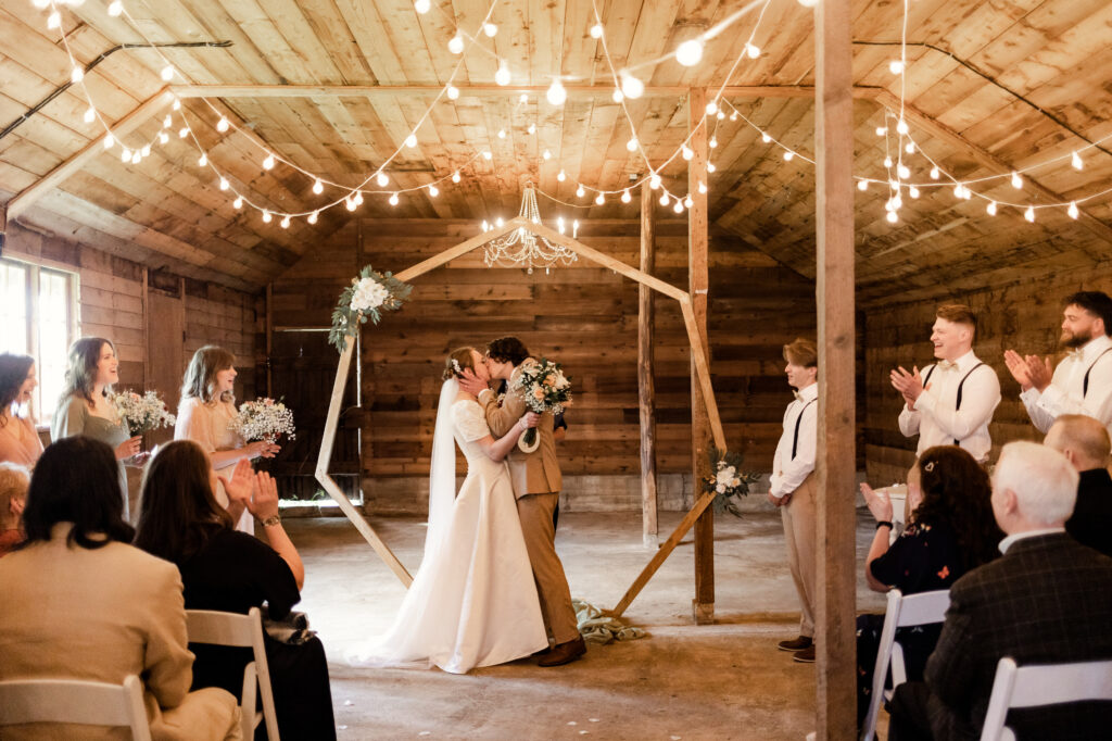 The bride and groom share a first kiss as their bridal party cheers from the side at this Estate 248 wedding in Langley, British Columbia