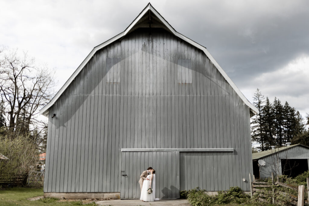 Bride and groom kiss in front of the blue barn at the blue barn at this Estate 248 wedding in Langley, British Columbia