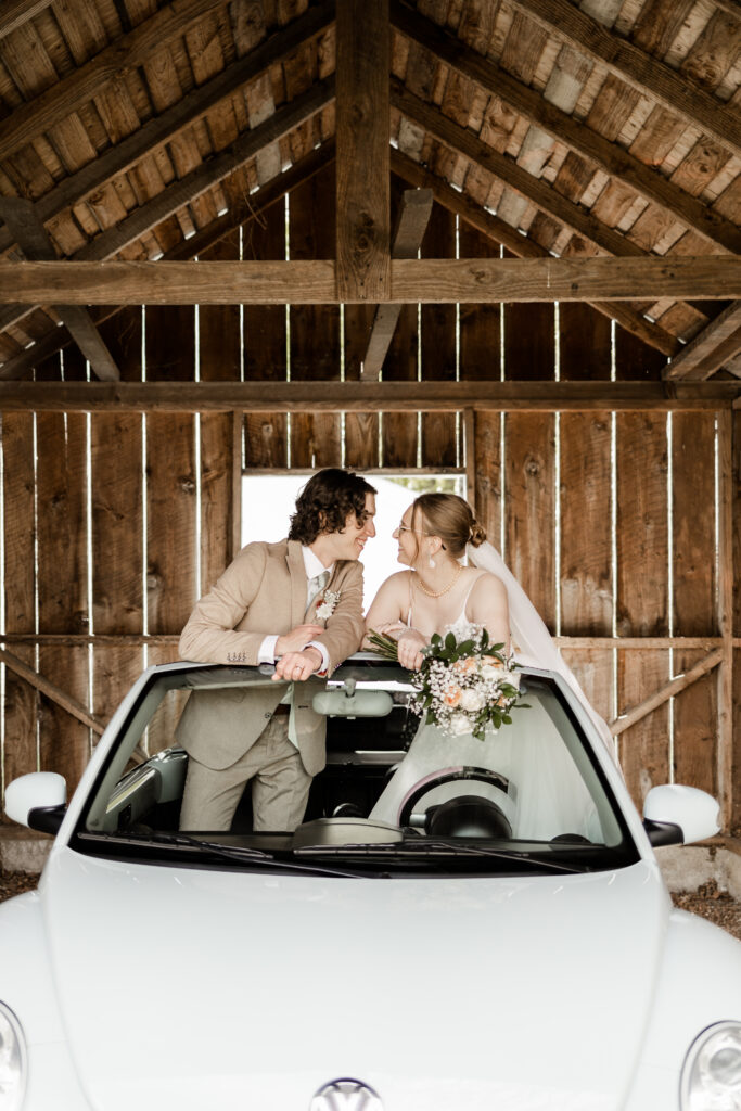 Bride and groom smile at each other as they stand inside a baby blue volkswagon at their Estate 248 wedding in Langley, British Columbia