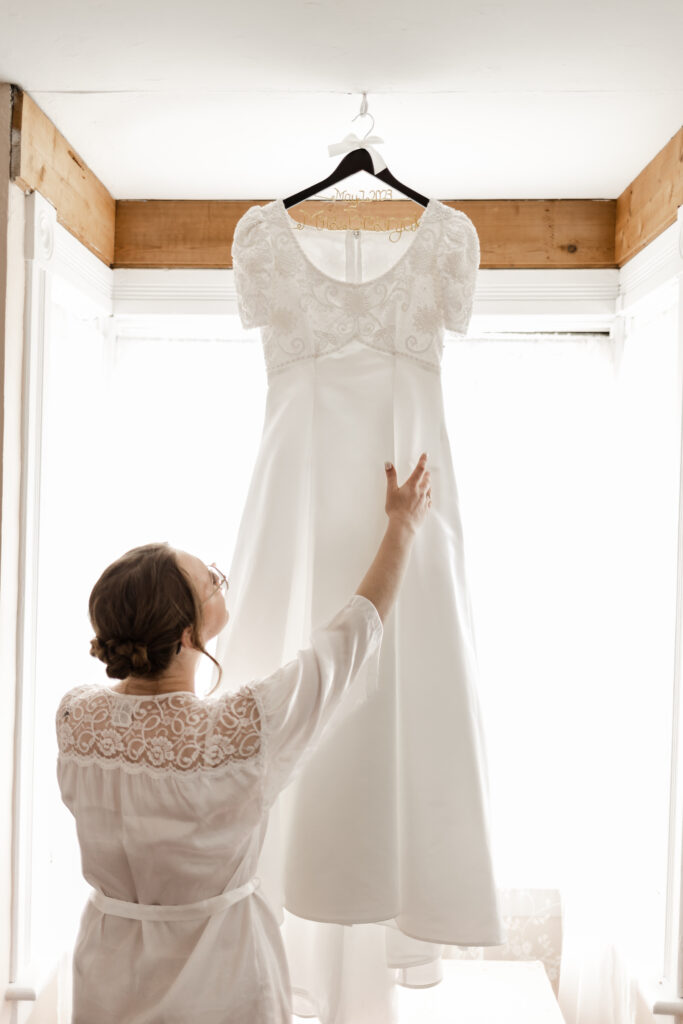 The bride adjusting her hanging dress in the window at this Estate 248 wedding in Langley, British Columbia