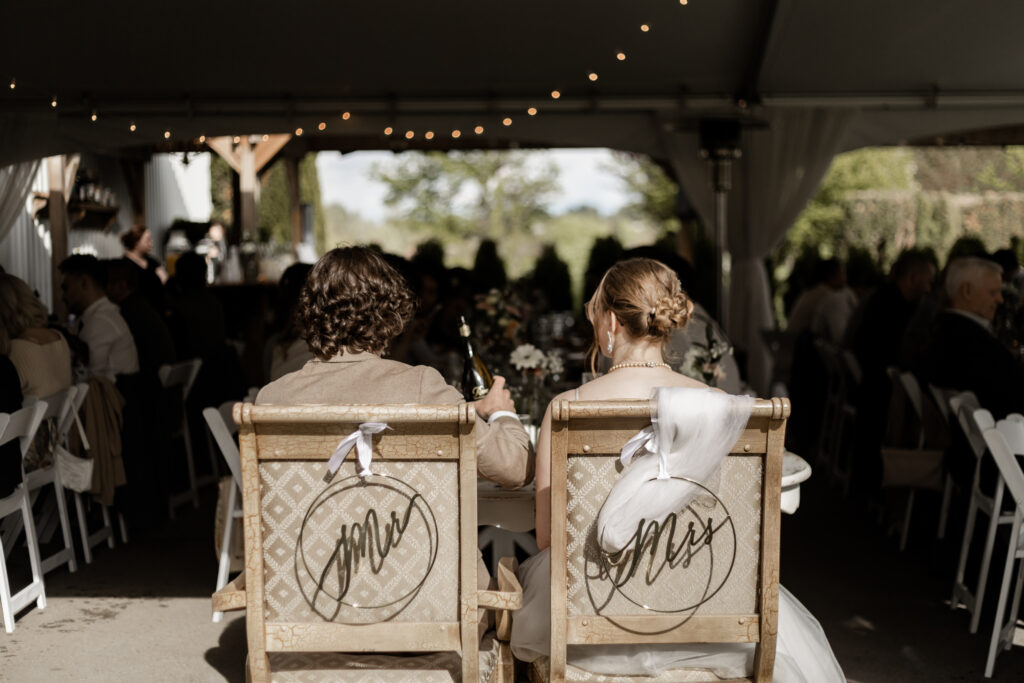 The bride and groom sit at the reception on chairs that say "Mr" and "Mrs" respectively at their Estate 248 wedding in Langley, British Columbia