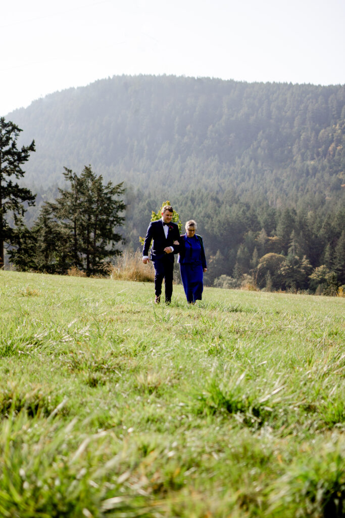 Groom walks down the aisle with his mother at this Bird's Eye Cove wedding