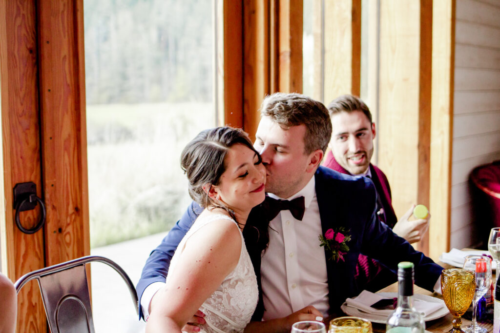 Groom kisses bride on cheek during their reception at this Bird's Eye Cove wedding