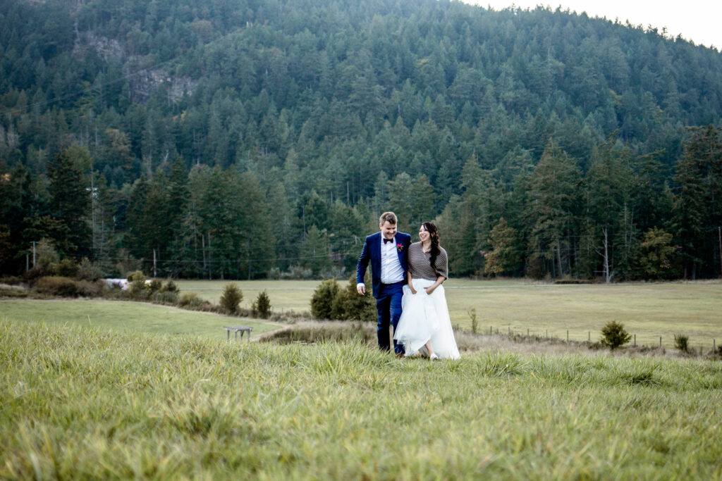 Bride and groom walk through the field during blue hour at this Bird's Eye Cove wedding